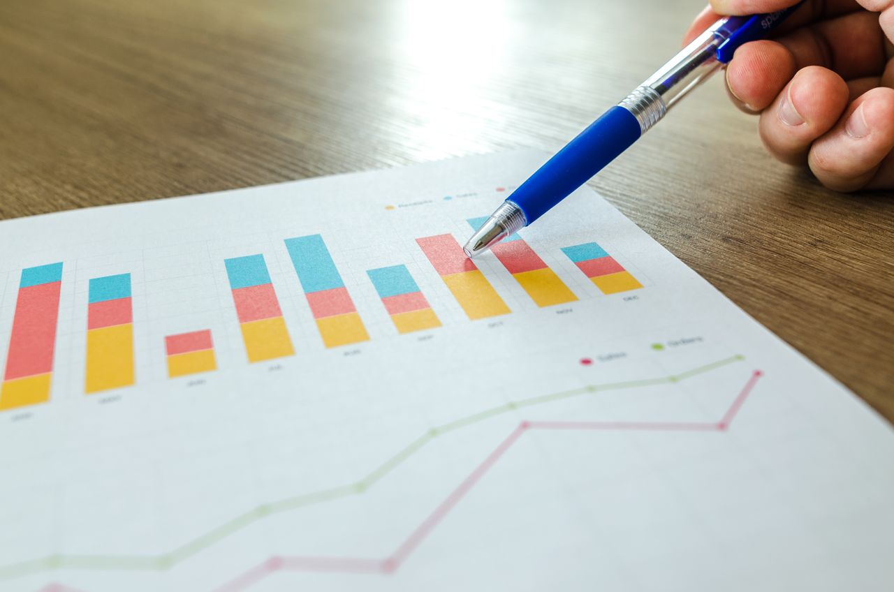 Vue rapprochée détaillée d’une main pointant des graphiques colorés avec un stylo bleu sur une surface en bois.